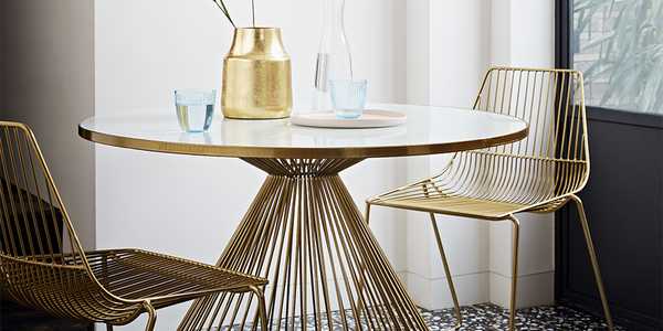 A gold and glass-topped round dining table with matching chairs and decor.